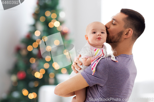 Image of father kissing baby daughter over christmas tree