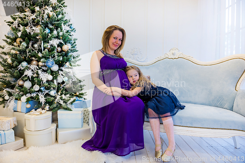 Image of Beautiful pregnant woman in ultra violet dress sitting with doughter