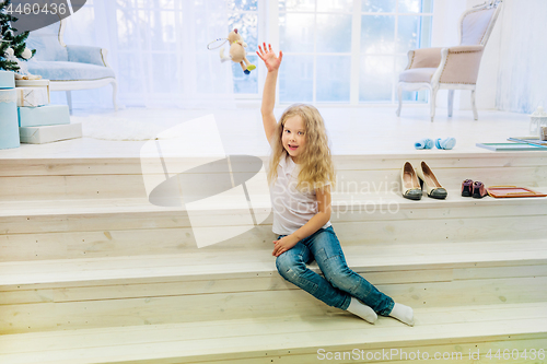 Image of Cute girl in in casual clothes sitting and playing on staircase