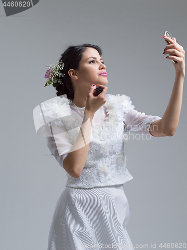 Image of bride paints lips with lipstick