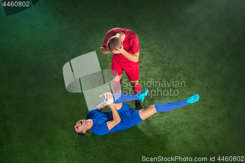 Image of Male soccer player suffering from leg injury on football green field