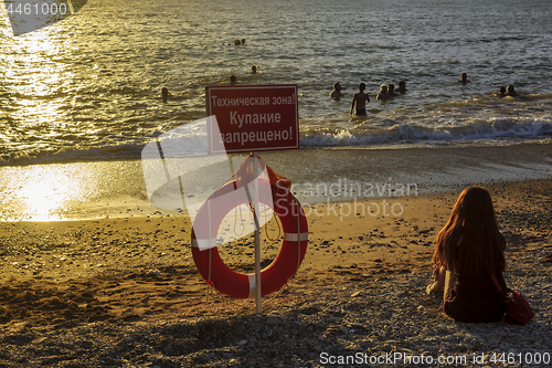 Image of People swim in sunset sea right at the prohibitory sign