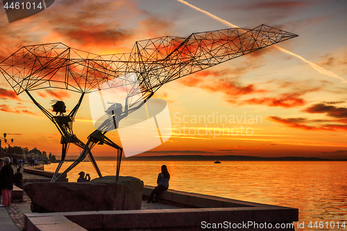 Image of Silhouettes sculpture of fishers on lake embankment at sunset