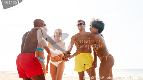 Image of happy friends stacking hands on summer beach