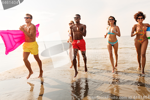 Image of friends run with beach ball and swimming mattress