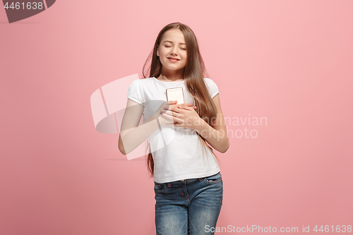 Image of The happy teen girl with phone standing and smiling against pink background.
