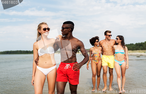 Image of mixed race couple walking along beach with friends
