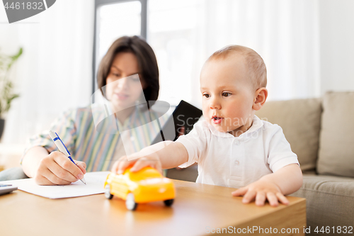 Image of baby playing with car and mother working at home