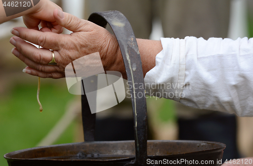 Image of Woman helps a child dip a candle wick into molten beeswax