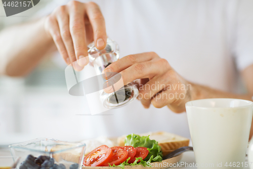 Image of close up of hands seasoning food by pepper mill
