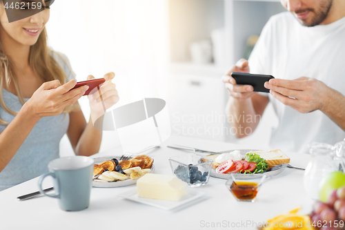 Image of close up of couple with smartphones at breakfast