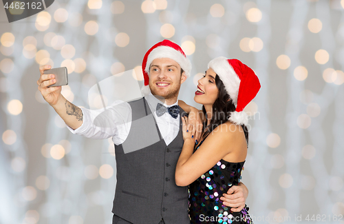 Image of couple in santa hats taking selfie at christmas