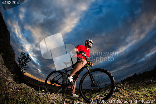 Image of cyclist standing with mountain bike on trail at sunset