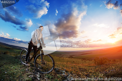 Image of cyclist standing with mountain bike on trail at sunset