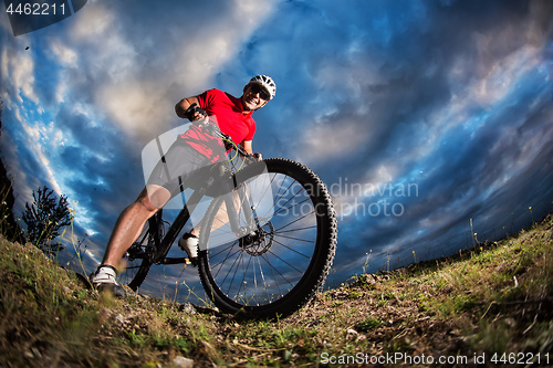 Image of cyclist standing with mountain bike on trail at sunset