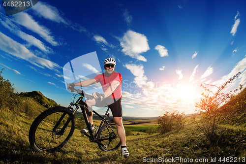 Image of cyclist standing with mountain bike on trail at sunset