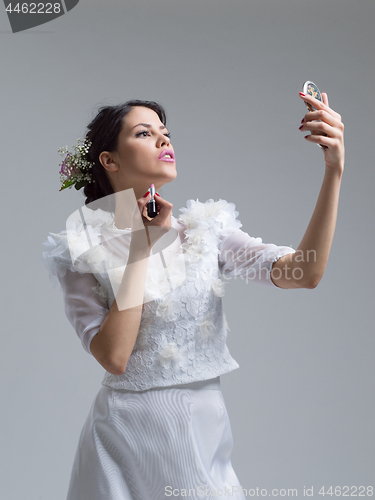 Image of bride paints lips with lipstick