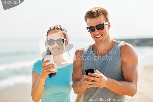 Image of couple in sports clothes with smartphones on beach