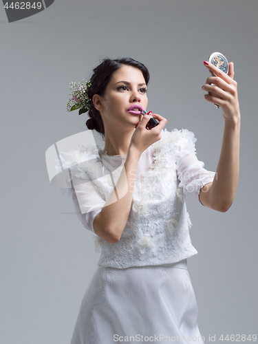 Image of bride paints lips with lipstick