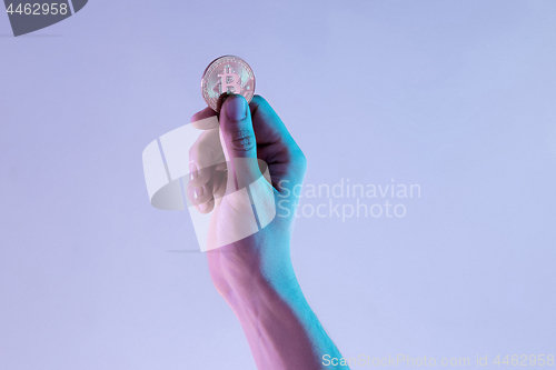 Image of Male hand with golden bitcoin on blue background