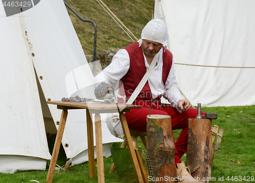 Image of Man dressed in Medieval clothes making metal armour 