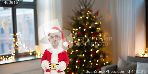 Image of unhappy man in santa clothes over christmas tree