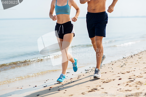 Image of couple in sports clothes running along on beach