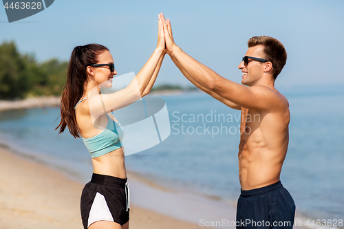 Image of happy couple in sports clothes and shades on beach