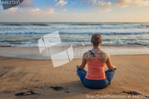 Image of Woman doing yoga oudoors at beach - Padmasana lotus pose