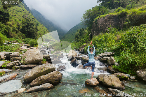 Image of Woman in yoga asana Vrikshasana tree pose at waterfall outdoors