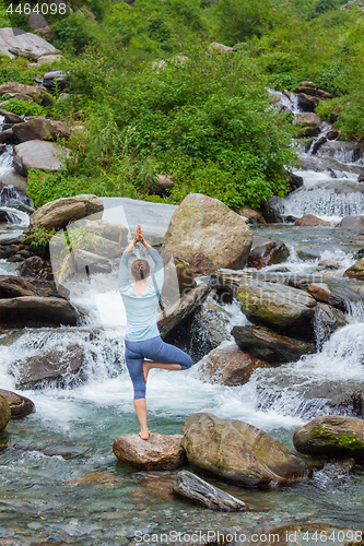 Image of Woman in yoga asana Vrikshasana tree pose at waterfall outdoors