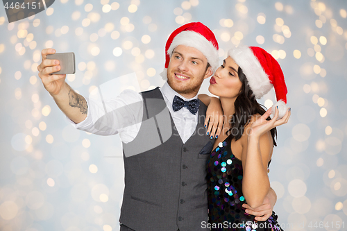 Image of couple in santa hats taking selfie at christmas