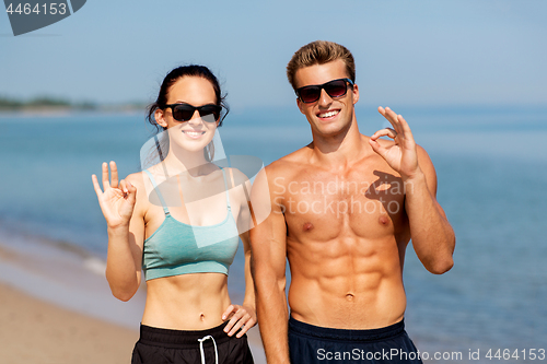 Image of couple of athletes in shades on beach showing ok