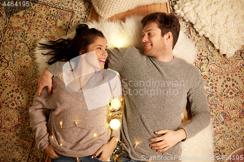 Image of happy couple with garland lying on floor at home