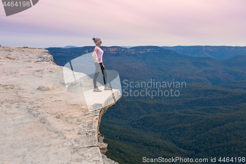 Image of Adventurous female standing on the mountain ledge looking out to the valley beyond