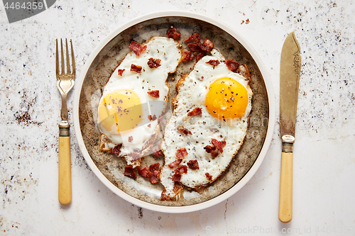 Image of Two fresh fried eggs with crunchy crisp bacon served on rustic plate