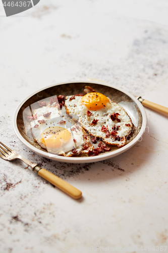 Image of Two fresh fried eggs with crunchy crisp bacon served on rustic p
