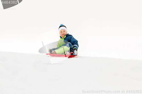 Image of happy boy sliding on sled down snow hill in winter