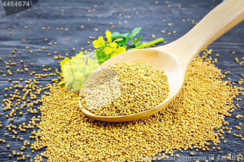 Image of Mustard seeds in wooden spoon with flower on black board