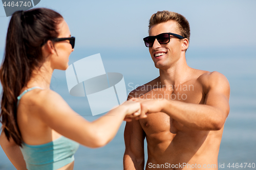 Image of happy couple in sports clothes and shades on beach