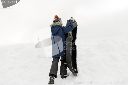 Image of little boy with sled climbing snow hill in winter