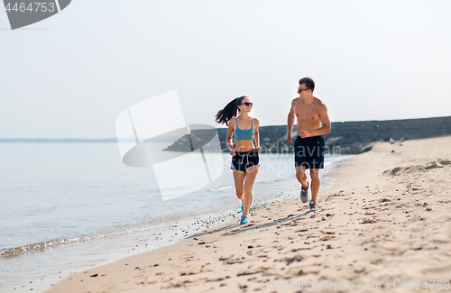 Image of couple in sports clothes running along on beach