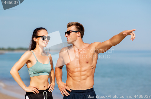 Image of happy couple in sports clothes and shades on beach