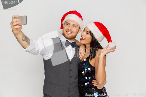 Image of couple in santa hats aking selfie at christmas