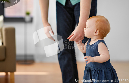 Image of baby girl walking with father help at home