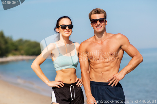 Image of happy couple in sports clothes and shades on beach