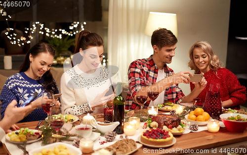 Image of friends with smartphones having christmas dinner