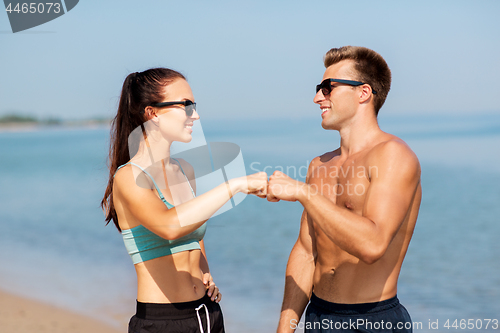 Image of happy couple in sports clothes and shades on beach