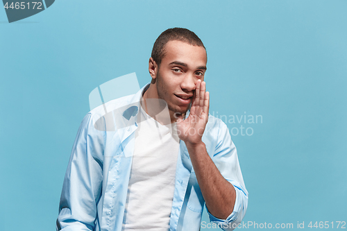 Image of The young man whispering a secret behind her hand over blue background