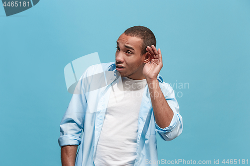 Image of The young man whispering a secret behind her hand over blue background